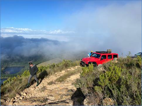 A person walking on a dirt road with a red jeep on a hill

Description automatically generated